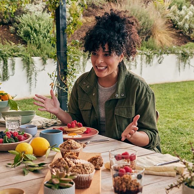 Woman smiling in front of an assortment of colorful fruits and vegetables on table